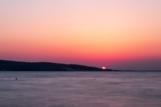 a long exposure wide landscape shoot of sea at sunset with good colors while sun sinking.