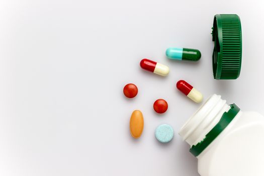 Multicoloured capsules with white medicine bottles and green caps on white background. Copy space for text or articles. Concepts of health and medicine.