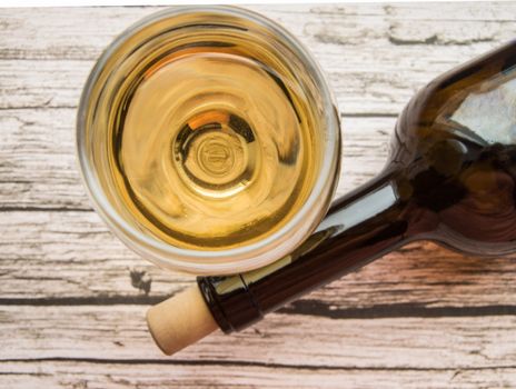 Top view of a glass of dry white wine and a bottle lying on an old wooden background.