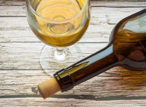 Top view of a glass of dry white wine and a bottle lying on an old wooden background.
