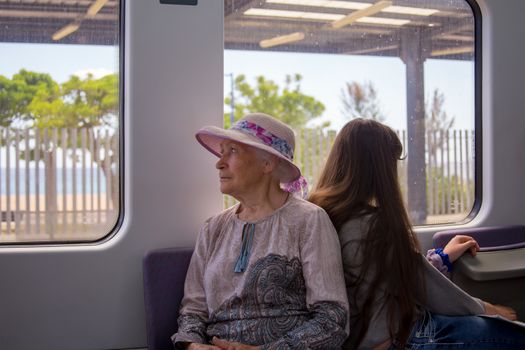 Beautiful gray-haired grandmother in a sunhat rides a commuter train and looks out the window.