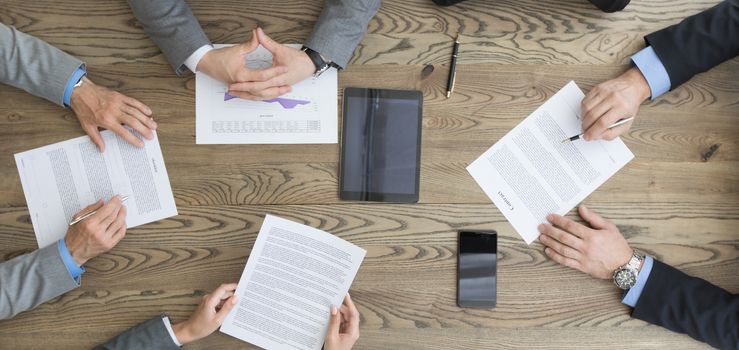 Business team working with contract, financial reports and mobile devices dicussing deal sitting around office table