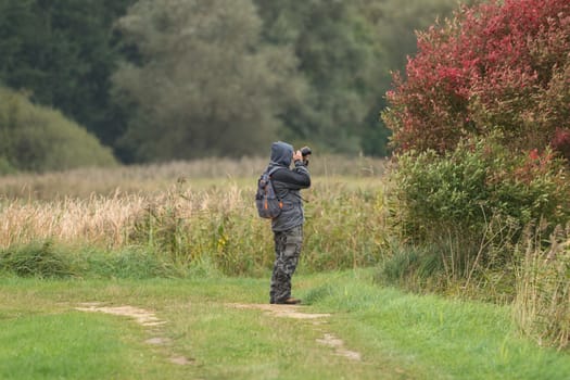 A man photographs something and stands in a meadow