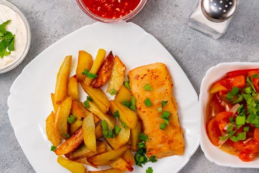 Fried fish and chips on a white plate on the kitchen table with tomato sauce, tartar sauce and pickled vegetables salad - photo, image. Flat lay, top view