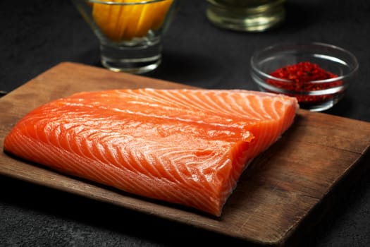 Piece of salmon fillet on a wooden cutting board with ingredients for its further preparation - photo, image.