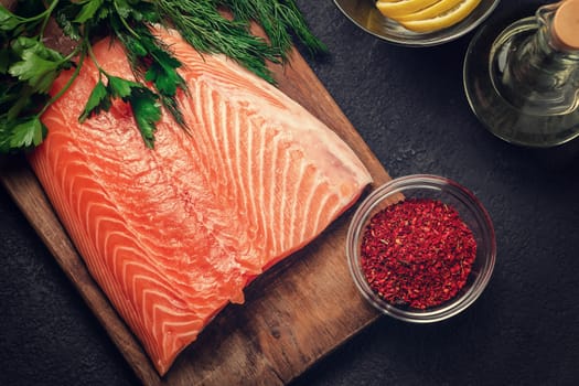 Piece of salmon fillet on a wooden cutting board with ingredients for its further preparation, top view - photo, image.