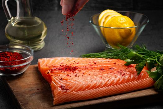 Female hand sprinkles a piece of salmon fillet lying on a wooden cutting board with spices - photo, image,