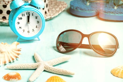 Seashells, alarm clock and beach accessories on a blue table - summer vacation and vacation time concept.