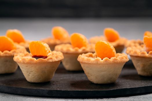 Sweet tartlets with chocolate and slices of tangerine on a dish of natural slate for serving.