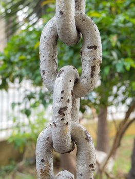 Close up of rusty chain links in foreground, with green on background