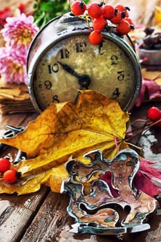 Autumn still life with an alarm clock and fallen leaves.