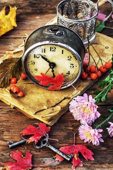 Autumn still life with an alarm clock and fallen leaves.