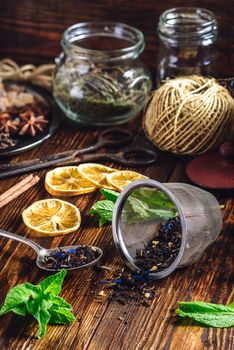 Dry Tea in Spoon and Strainer, Fresh Mint and Lemon Slices. Tangle with Two Jars and Teapot on Backdrop.