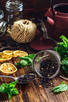 Dry Tea in Strainer and Spoon with Fresh Mint and Lemon Slices. Tangle with Two Jars and Teapot on Backdrop.