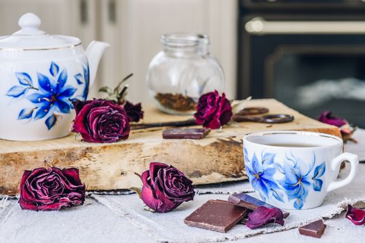 Cup of Tea with Chocolate Bars, Dry Rosebuds and Teapot with Jar and Rusty Scissors on Board.