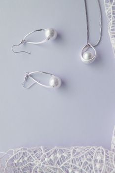 Beautiful silver shiny pearl jewelry, trendy glamorous earrings, chain on delicate pastel background with exquisite lace. Lay flat, top vertical frame.