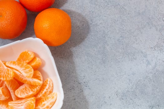 Several whole and peeled ripe tangerines on a white plate on gray background with space for text, flat lay, top view.