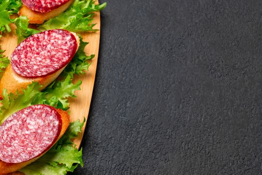 Several sandwiches with sausage and salami and sauce on a black board, flat lay background with copyspace.