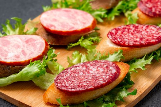 Several sandwiches with sausage and salami and sauce on a black board, flat lay background with copyspace.