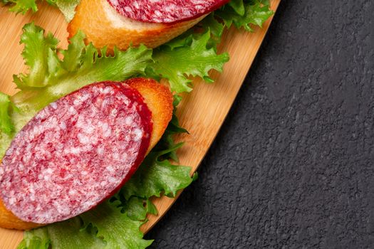 Several sandwiches with sausage and salami and sauce on a black board, flat lay background with copyspace.