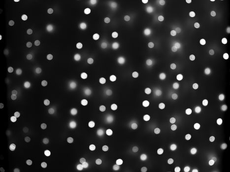 Defocused lights of Christmas garland in black and white evenly distributed over the area of the frame, background, texture.