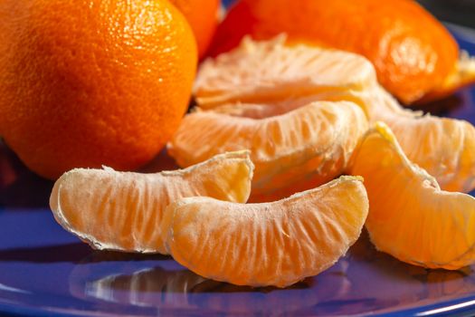 Several whole and peeled ripe tangerines on a blue plate.