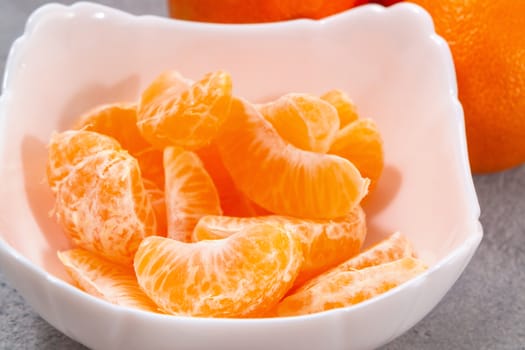 Several whole and peeled ripe tangerines on a white plate on gray background.
