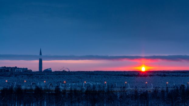 Colorful sunset in the cloudy sky over a snowy forest on the outskirts of the city.