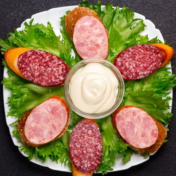 Several sandwiches with sausage and salami and sauce on a plate, flat lay.