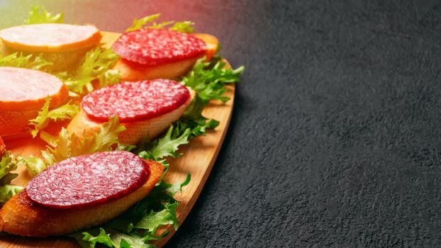 Several sandwiches with sausage and salami and sauce on a black board, flat lay background with copyspace.