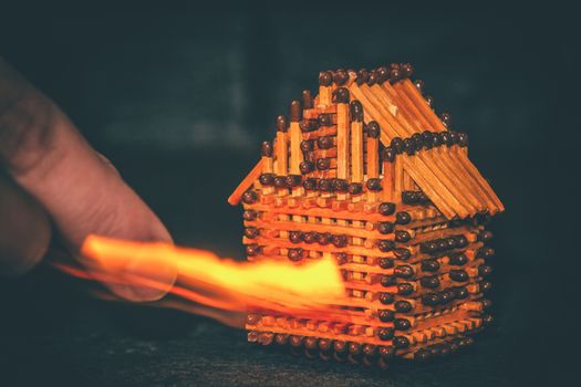 hand with a burning match sets fire to the house model of matches, risk, property Insurance protection or ignition of combustible materials concept.