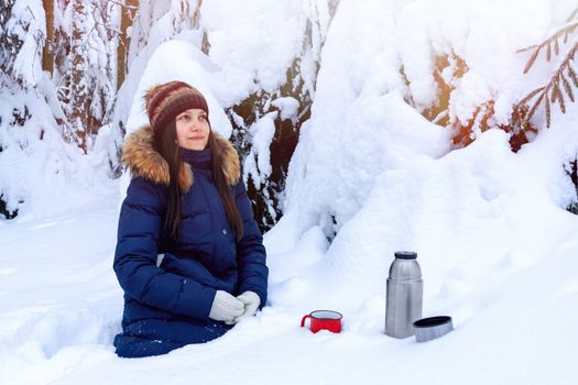 girl drinks coffee from a thermos while walking through a snowy winter forest.