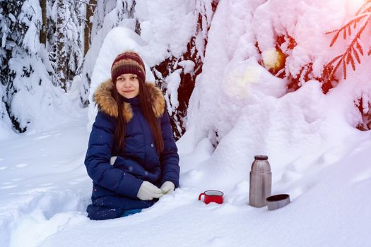 girl drinks coffee from a thermos while walking through a snowy winter forest.