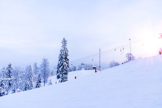 Snow-covered ski slope in the mountains with a lift and skiers skating away.