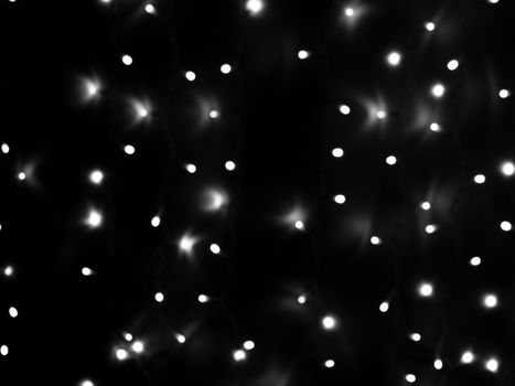 Defocused lights of Christmas garland in black and white evenly distributed over the area of the frame, background, texture.