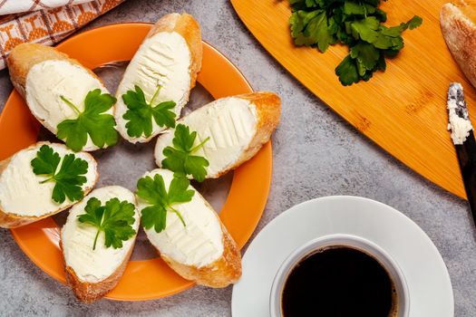 Freshly made sandwiches with cream cheese and parsley on a plate, chopping wooden board and a cup of coffee - morning and breakfast concept, top view.