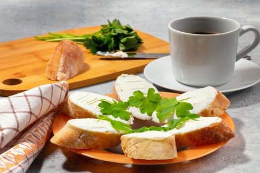 Freshly made sandwiches with cream cheese and parsley on a plate, chopping wooden board and a cup of coffee - morning and breakfast concept.