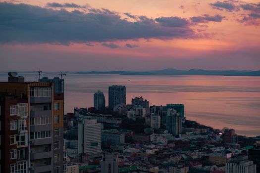 View of the city of Vladivostok from the hill eagle's nest . Sunset. The sky is orange and pink. Sea and city at sunset.