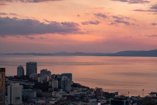 View of the city of Vladivostok from the hill eagle's nest . Sunset. The sky is orange and pink. Sea and city at sunset.