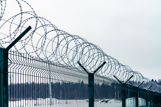 Metal fence with barbed wire on top against the sky.