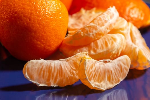 Several whole and peeled ripe tangerines on a blue plate.