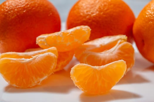 Several whole and peeled ripe tangerines on a white plate.