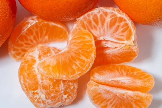 Several whole and peeled ripe tangerines on a white plate.