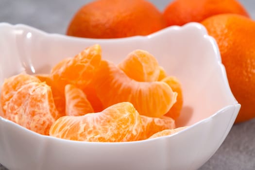 Several whole and peeled ripe tangerines on a white plate on gray background.