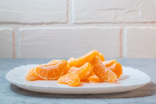 few peeled tangerine slices on white plate on the grey surface of the table, space for text.