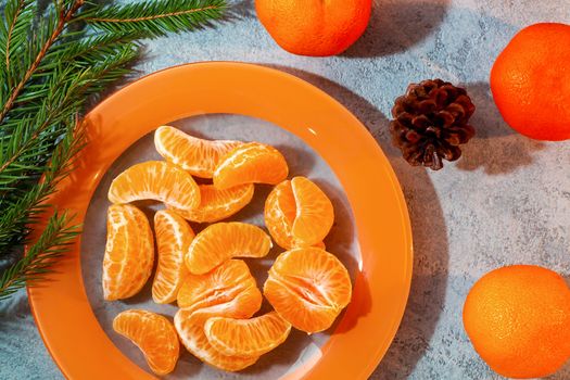 Several peeled tangerine slices on an orange plate with tree branches and a cone-a traditional Christmas and new year's composition in Russia.