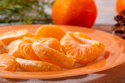 Several peeled tangerine slices on an orange plate with tree branches and a cone-a traditional Christmas and new year's composition in Russia.