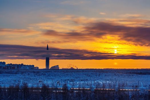 Colorful sunset in the cloudy sky over a snowy forest on the outskirts of the city.