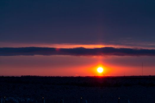 Colorful sunset in the cloudy sky over a snowy forest on the outskirts of the city.