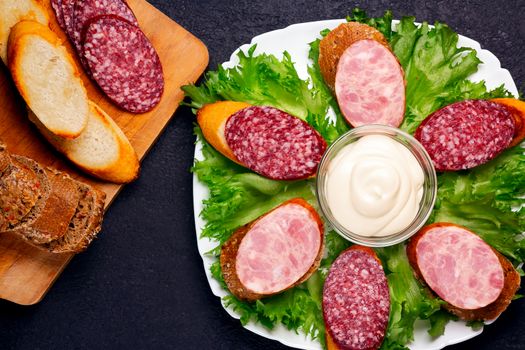 Several sandwiches with sausage and salami and sauce on a plate, flat lay.